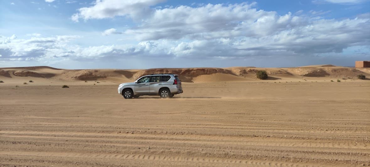A silver 4x4 crossing the sand below the dunes