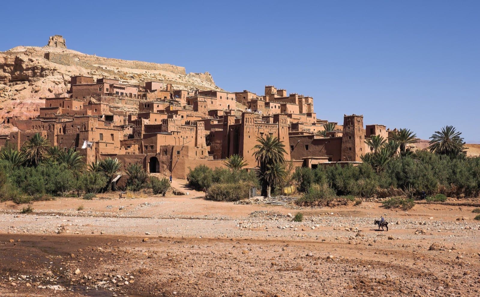 The rammed-earth ksar of Aït Benhaddou rising above palms and a dry riverbed